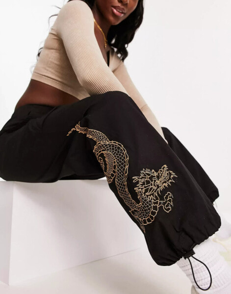 New Look embroidered dragon parachute trousers in black