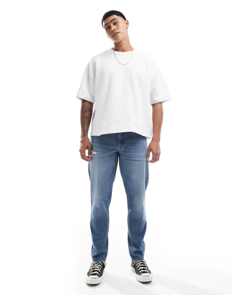 ASOS DESIGN tapered jeans with abrasions in midwash blue